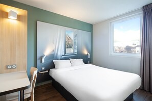 A hotel room with a large bed, a desk, and a window with curtains. - B&B HOTEL MEAUX (Meaux)