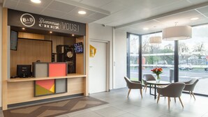 A hotel reception area with a modern design, featuring a reception desk, a digital screen, and a seating area with a table and chairs.