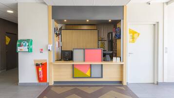 A reception area with a wooden desk, a fire extinguisher, a green waste bin, and a yellow directional sign.