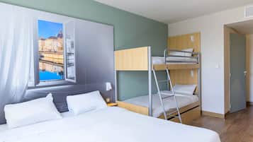 Hotellihuone, jossa on suuri sänky, kerrossänky, ikkuna, josta on näkymä rakennuksiin, ja ovi.