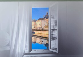 Una ventana abierta con vista a un edificio y un reflejo en el agua.