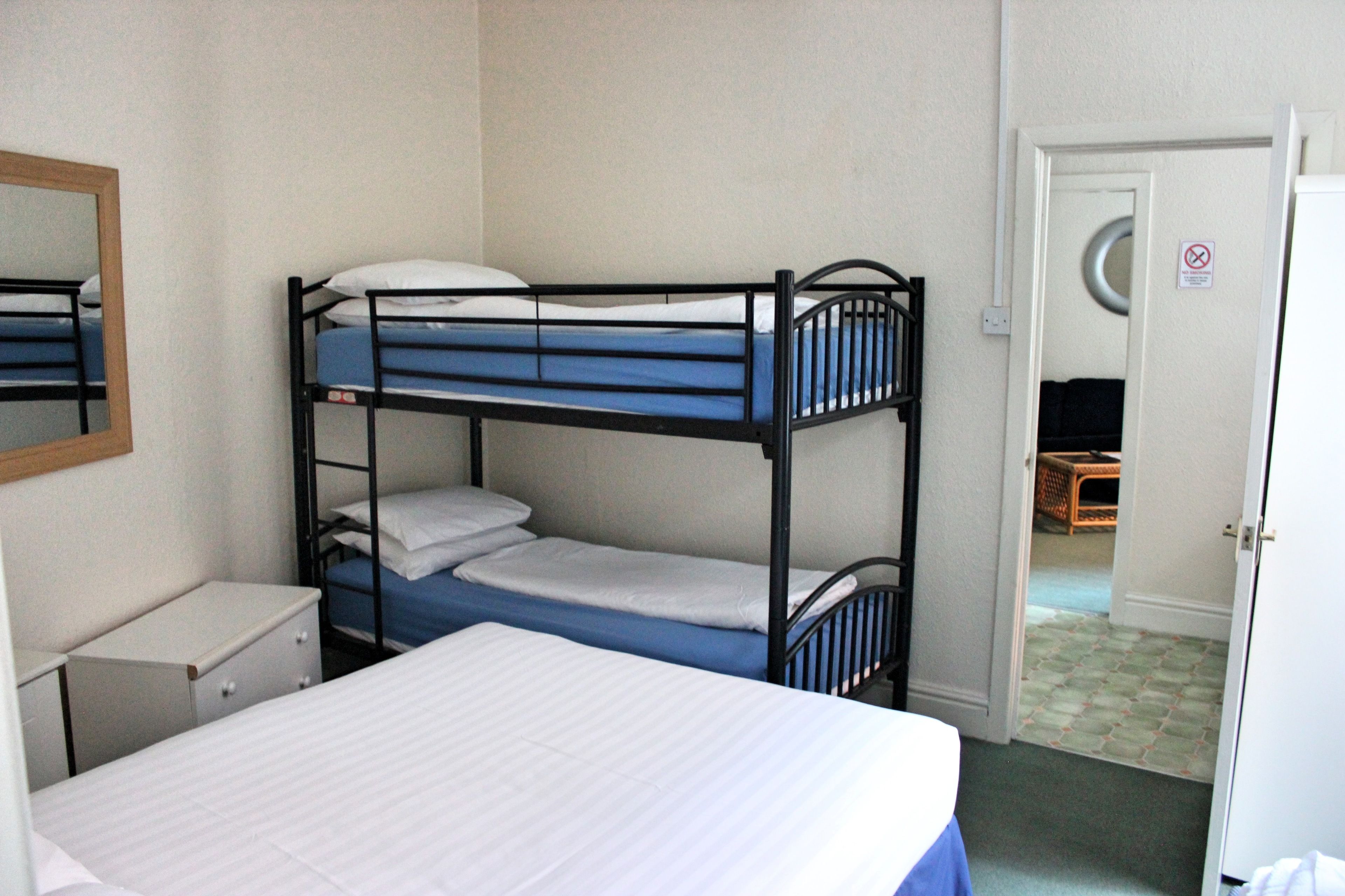 A bunk bed room with a mirror, a desk, and a door leading to another room.