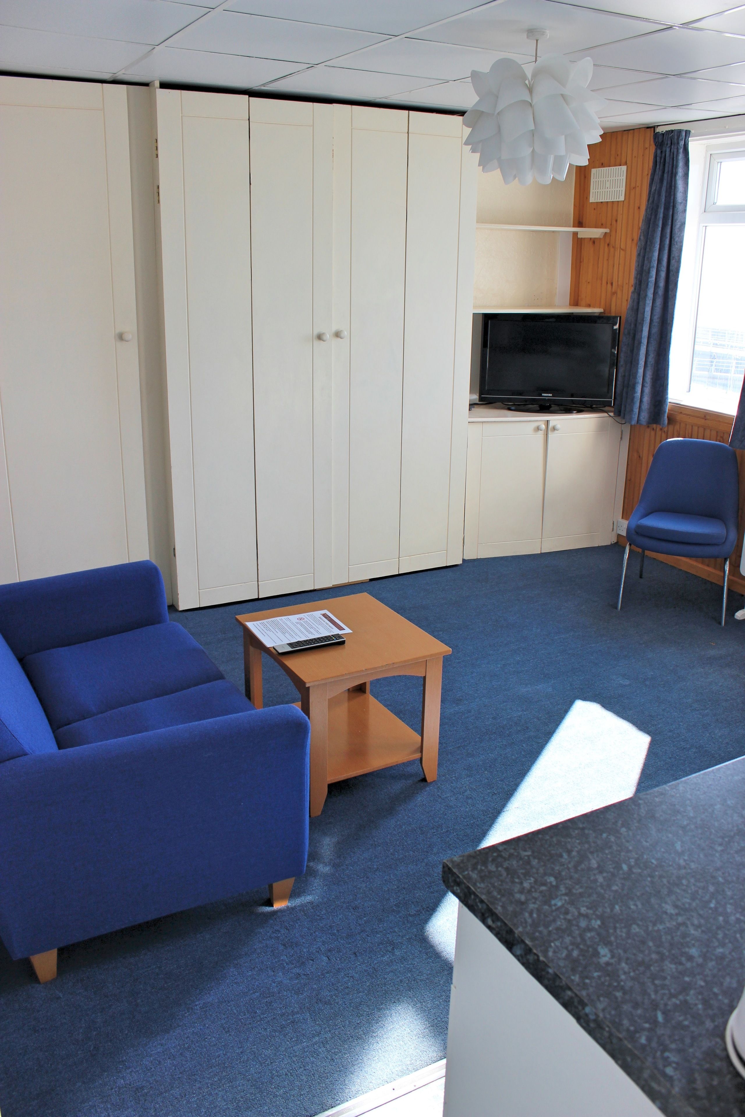 A room with a blue sofa, a small wooden table, a TV on a cabinet, and a blue chair.