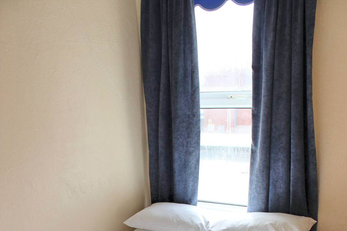 Un lit simple avec une literie blanche, une tête de lit en bois et une fenêtre avec des rideaux.