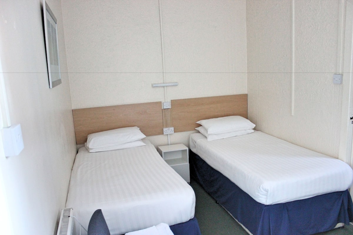 Une chambre d’hôtel avec deux lits simples, une tête de lit en bois, une petite table de chevet et un climatiseur fixé au mur.