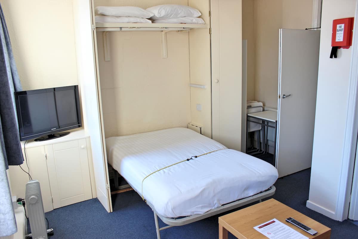 Une petite chambre d’hôtel comprenant un lit, une télévision, un bureau et une armoire.
