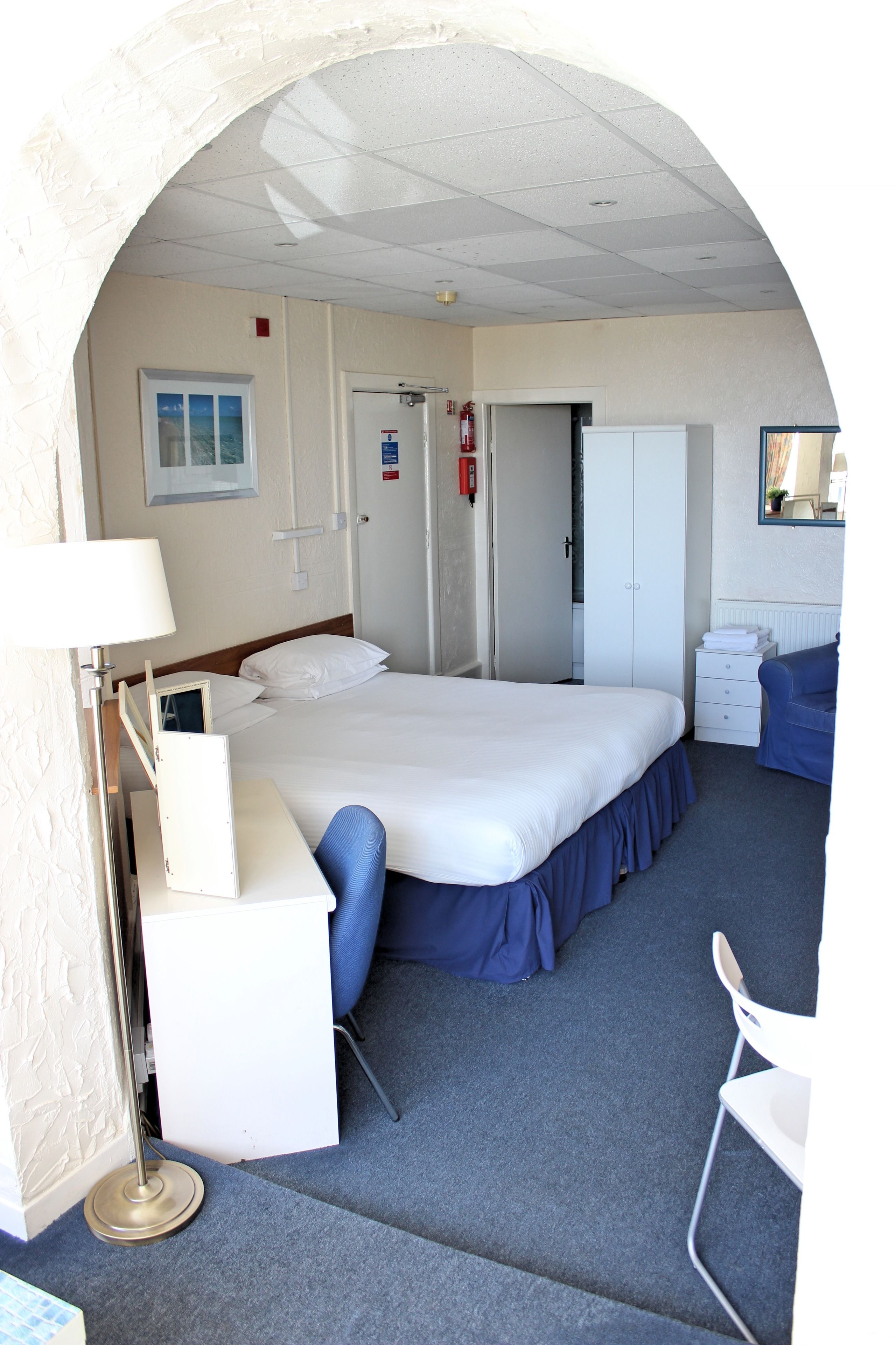 Une chambre d’hôtel comprenant un lit, un bureau, une chaise, une armoire et un miroir.