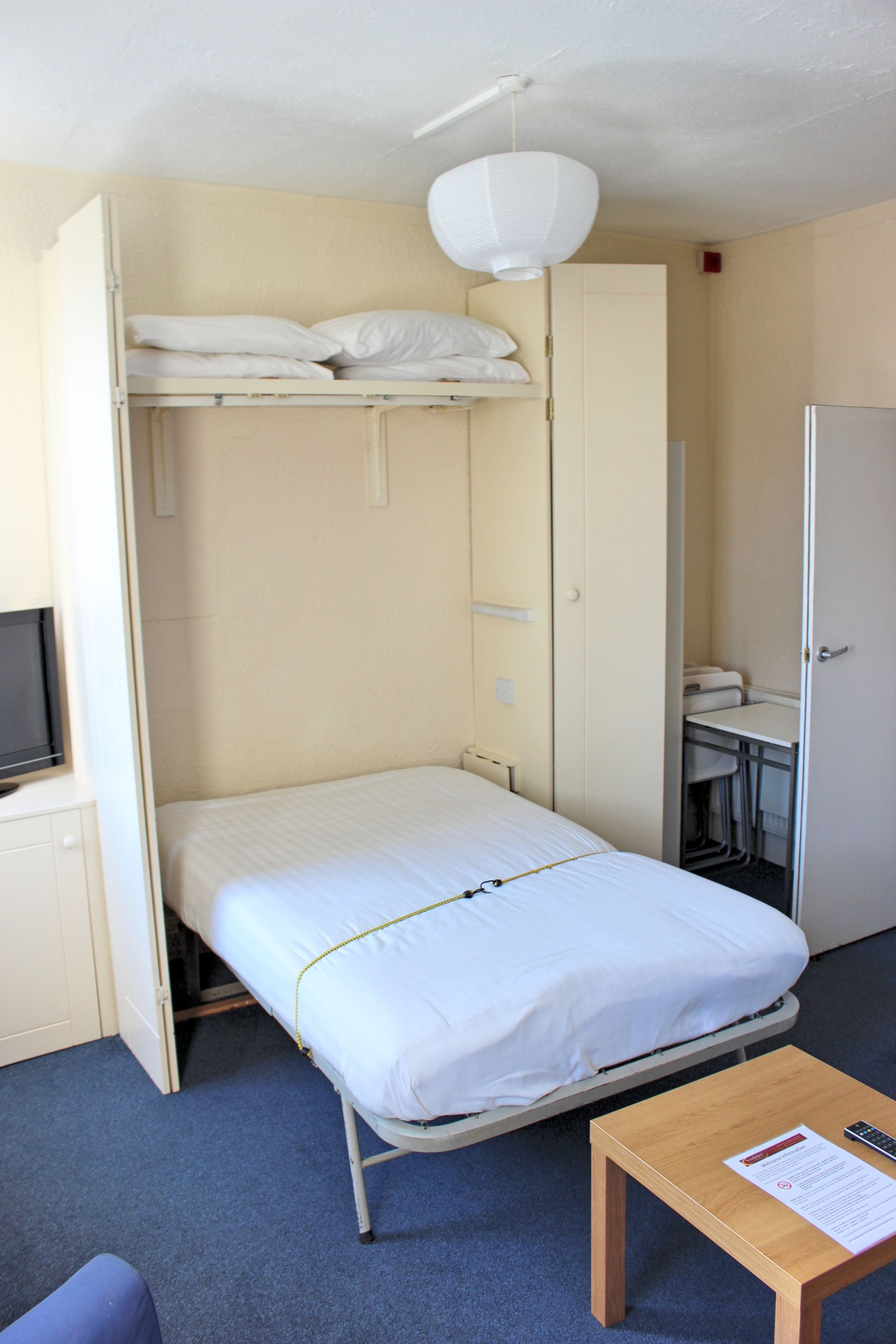 A compact hotel room with a single bed, a desk, a chair, a television, and a wardrobe.