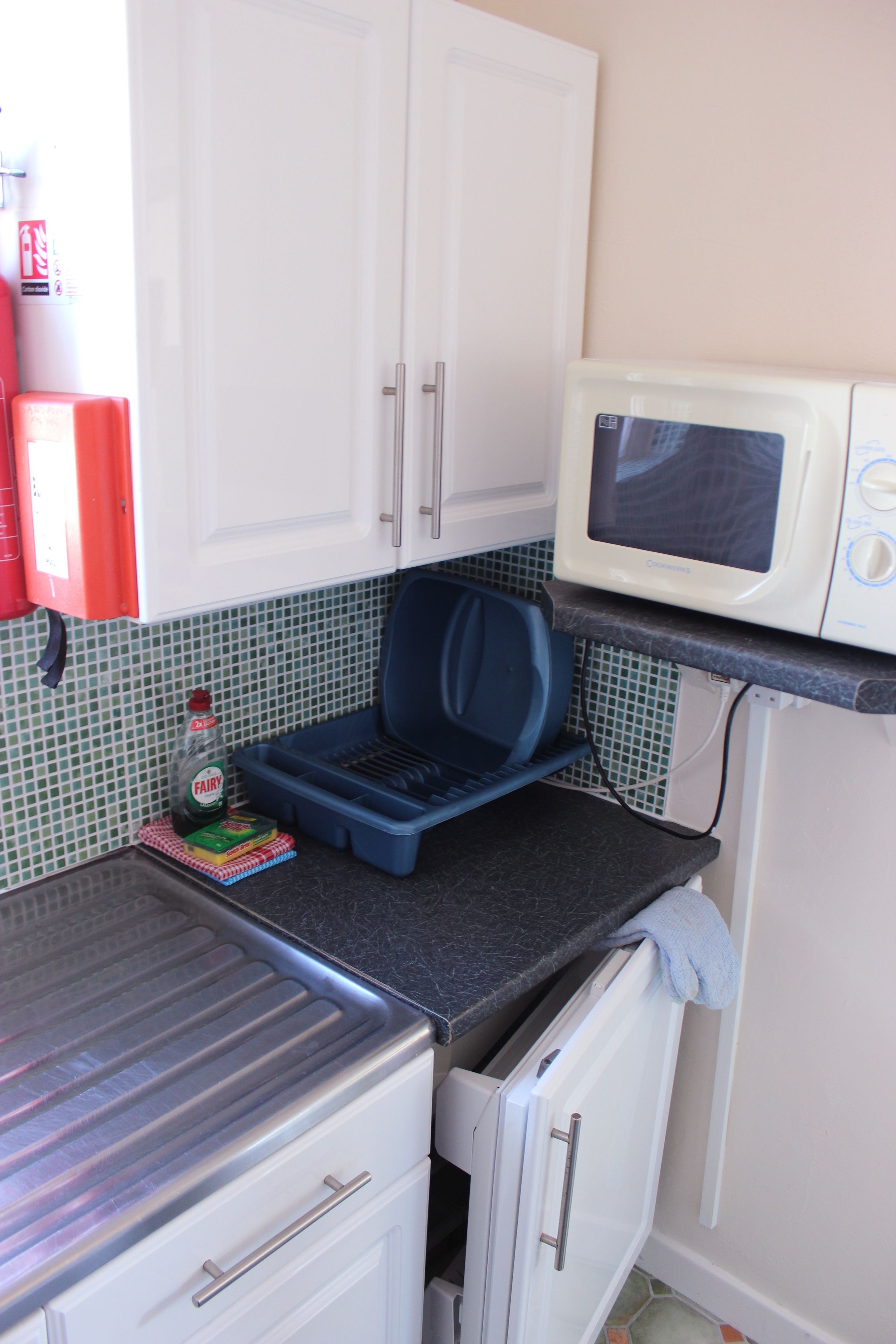 A compact kitchen with white cabinets, a microwave, a toaster, and a blue plastic container.