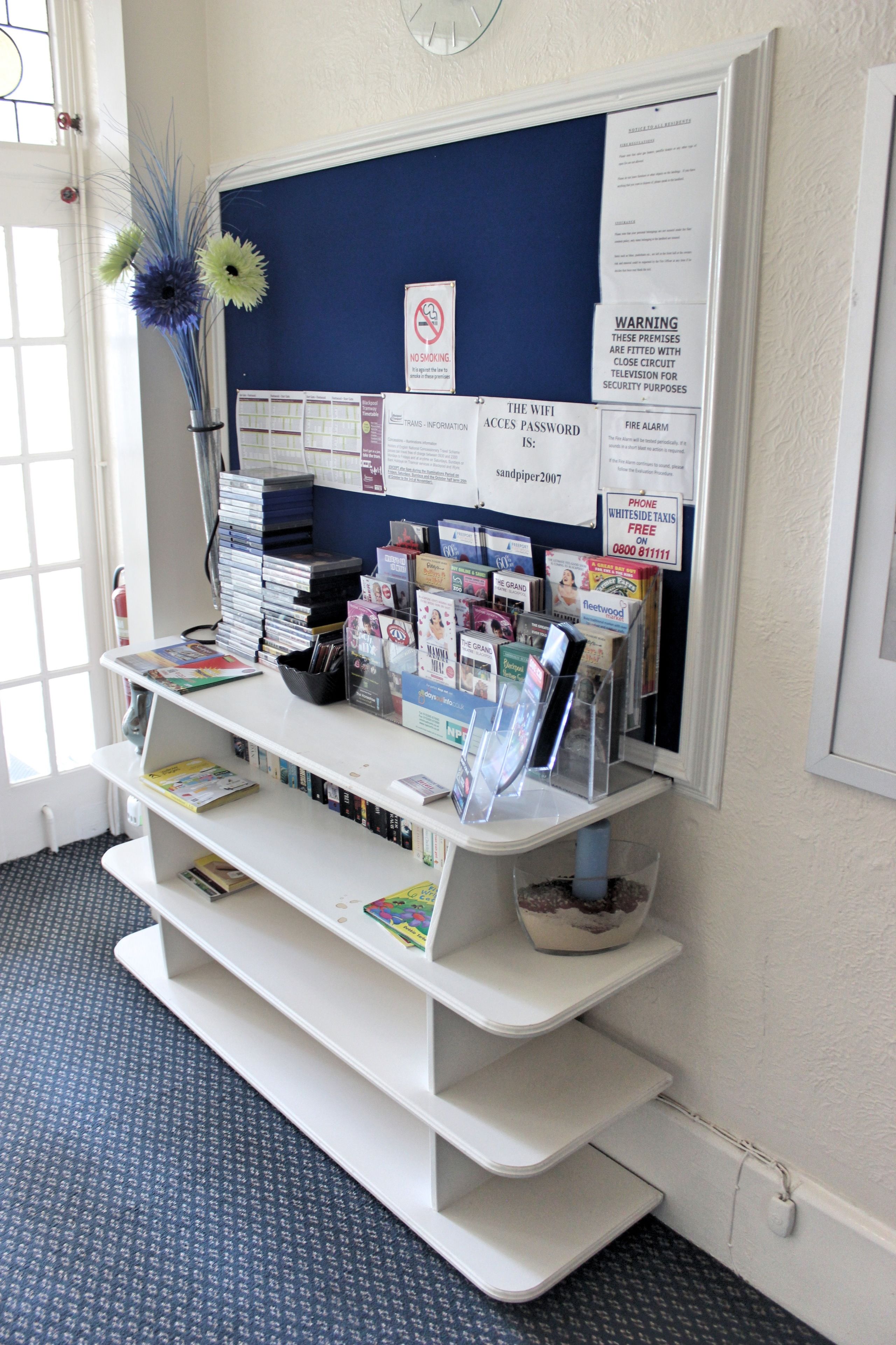 A reception desk with a bulletin board, magazines, and a vase with flowers.