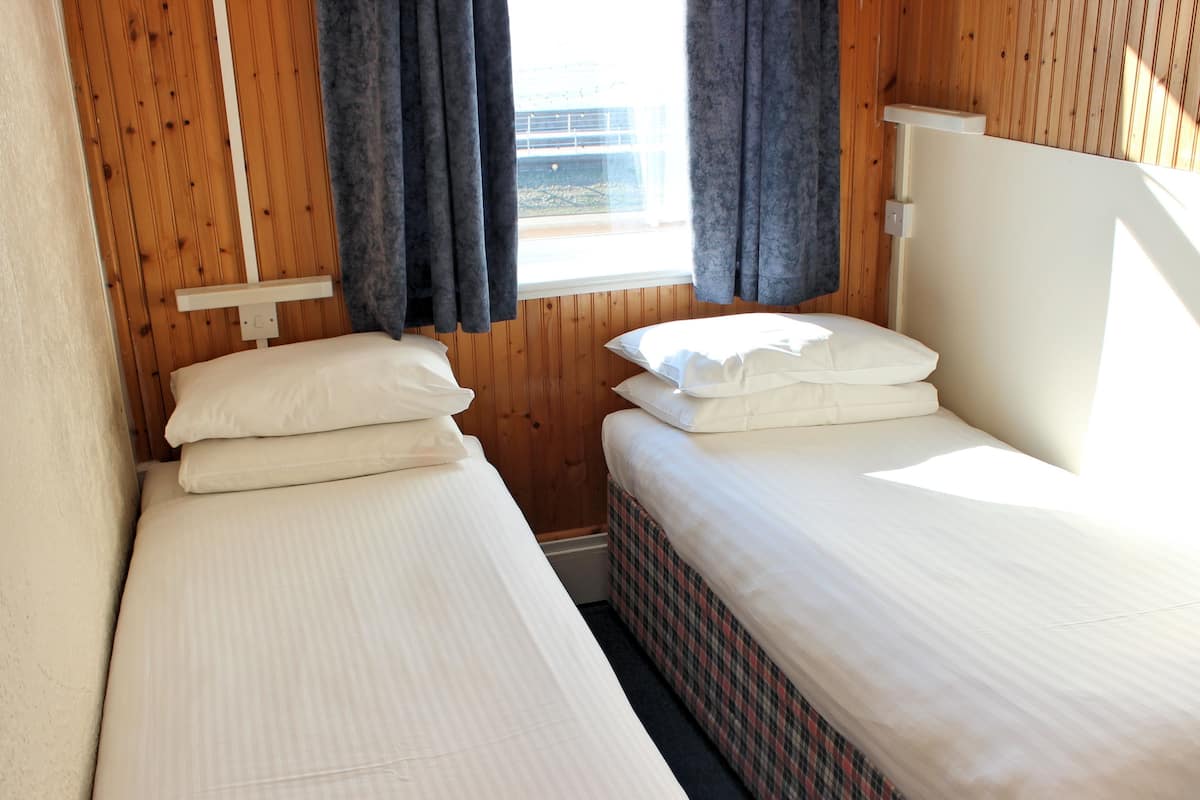 Une chambre avec deux lits, des murs en bois et une fenêtre avec des rideaux.
