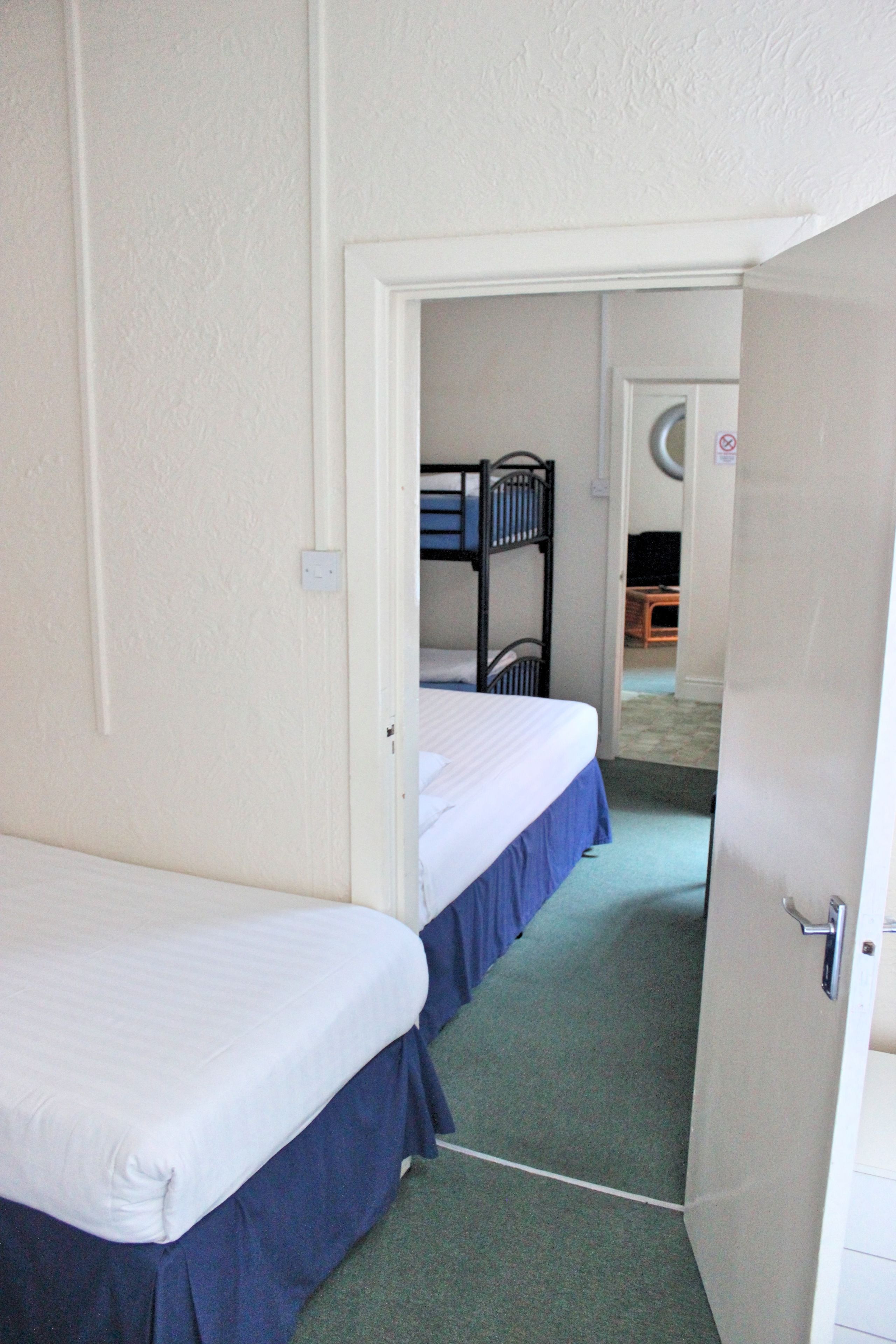 A narrow corridor with two single beds, each with a blue skirt and white bedding.