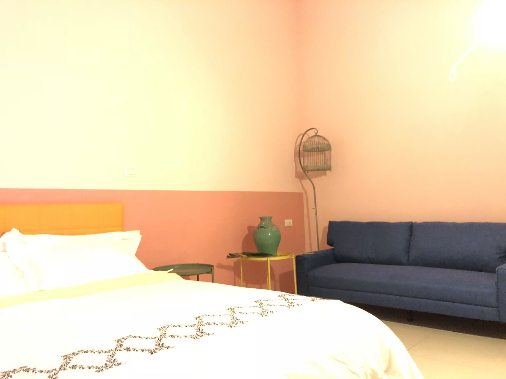 Un dormitorio con una cama, un sofá azul, un jarrón verde y una lámpara de pie.