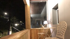 A balcony with a wooden railing, a table, two chairs, and a view of the city at night.