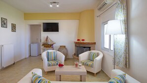 A living room with two white sofas, a coffee table, a fireplace, and a television mounted on the wall. - Laconia Domus - Papadianika (Monemvasia)