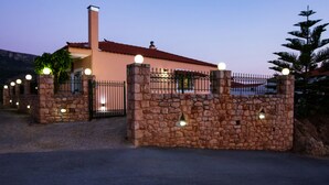 A stone-walled building with a red-tiled roof, a chimney, and a gated entrance with lights. - Laconia Domus - Papadianika (Monemvasia)