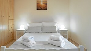 A neatly made bed with striped bedding, two bedside tables with lamps, and a wooden wardrobe. - Laconia Domus - Papadianika (Monemvasia)