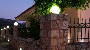 A stone wall with a metal fence and a tree with lights. - Laconia Domus - Papadianika (Monemvasia)