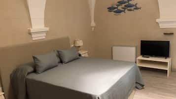 Quarto com cama, televisão sobre suporte, pequena mesa com abajur e decoração de peixes na parede.