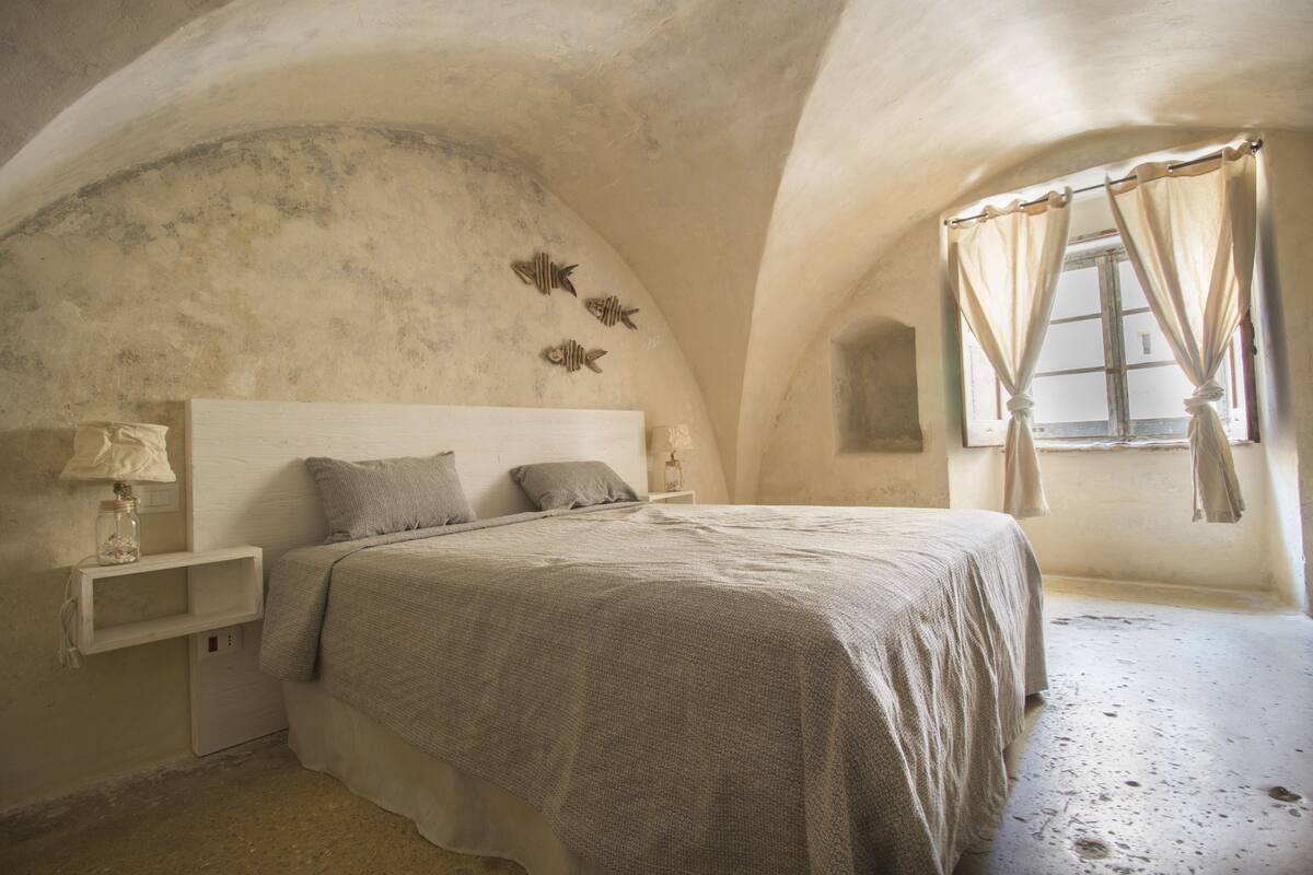 Un dormitorio con una cama individual, una mesita de noche, una lámpara y un ventanal con cortinas.