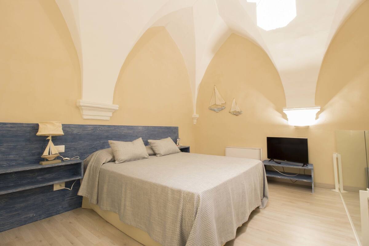 Un dormitorio con una cama, un televisor y una estantería con un modelo de barco.