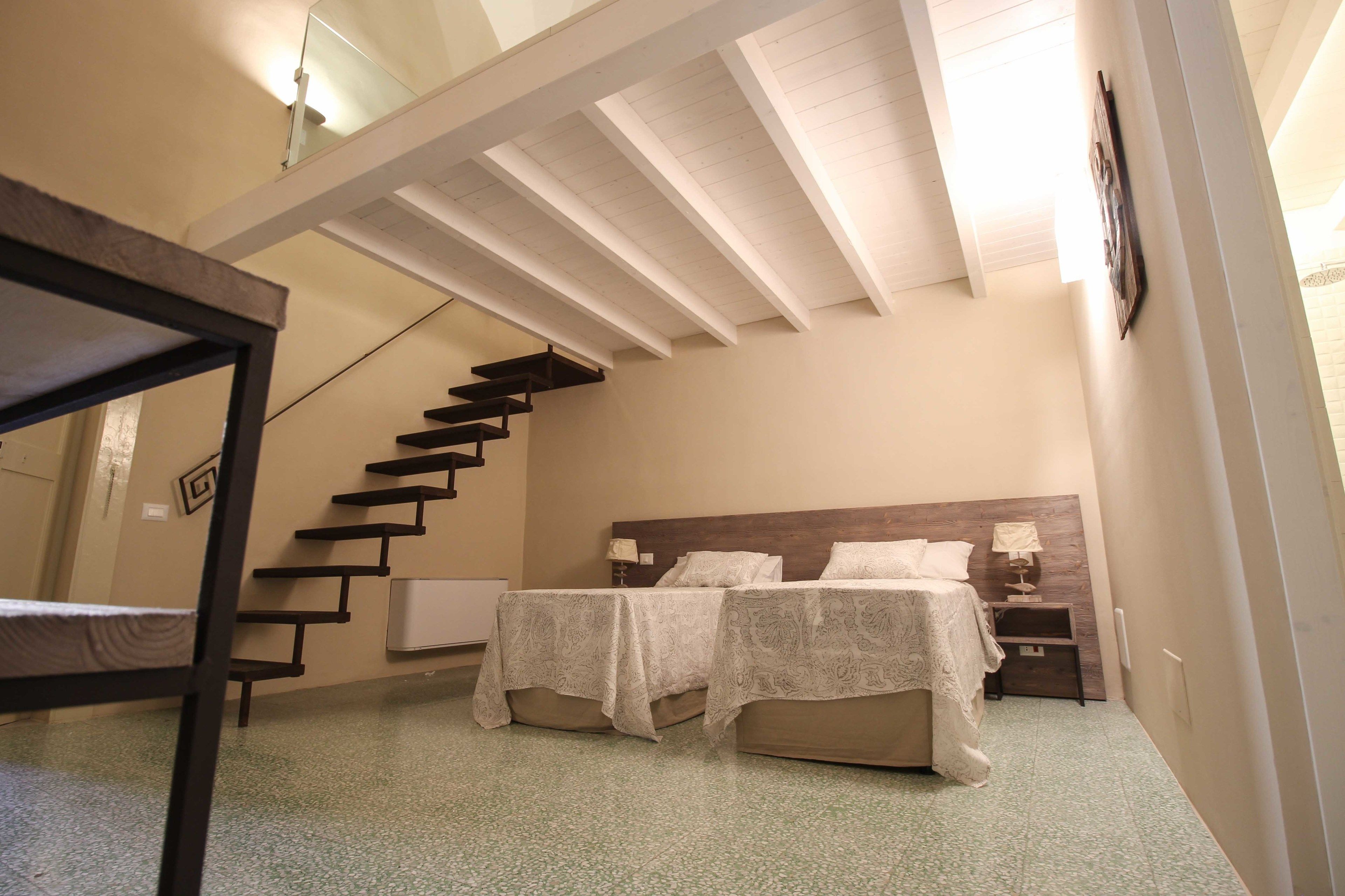A bedroom with two beds, a wooden staircase, and a nightstand with a lamp.