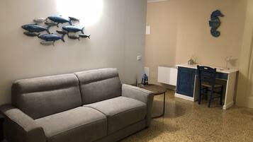 A living room with a grey sofa, a small round table, a desk with a chair, and wall decorations including fish and a seahorse.