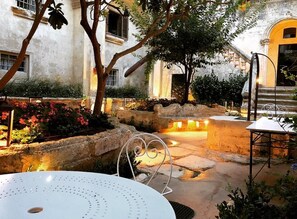 Un espace extérieur aménagé en patio, avec un banc en pierre, une table et une structure décorative en métal en forme de spirale.