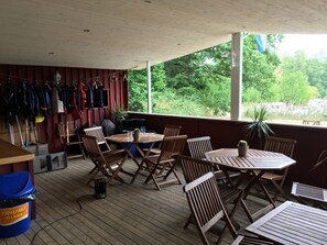 A covered patio with wooden furniture, a table with chairs, and a view of greenery outside. - Torne Camping (Lönashult)