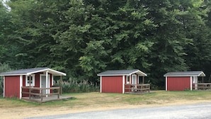 Three red cabins with porches and picnic tables, surrounded by a forest. - Torne Camping (Lönashult)