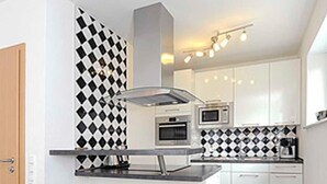A compact kitchen with a central island, two bar stools, a microwave, and a stove.