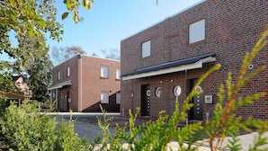 A modern brick building with a flat roof and a black door. There are windows on the second floor and a small sign on the door.
