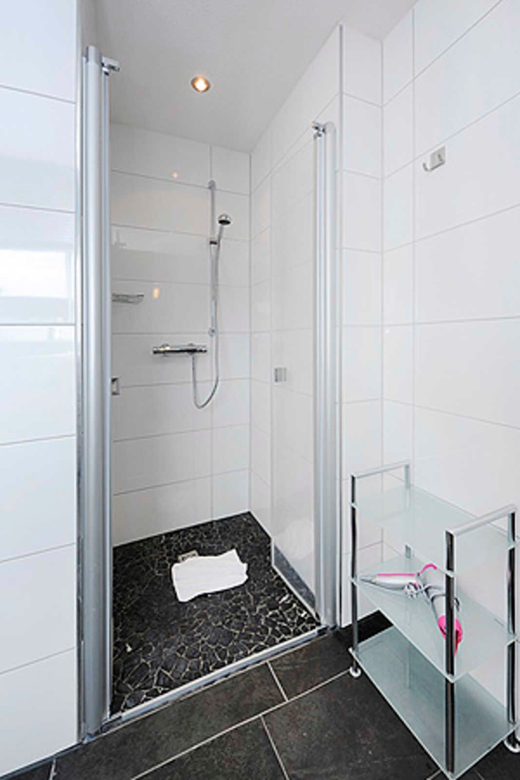 Een moderne badkamer met een douchecabine van glas, een vloer van marmertegel en een glazen wastafel met een roze handdoek.