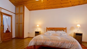 A bedroom with a wooden bed, two bedside lamps, a red and orange rug, and a wooden wardrobe. - Old Olive Mill House by TrulyCyprus (Dhoros)