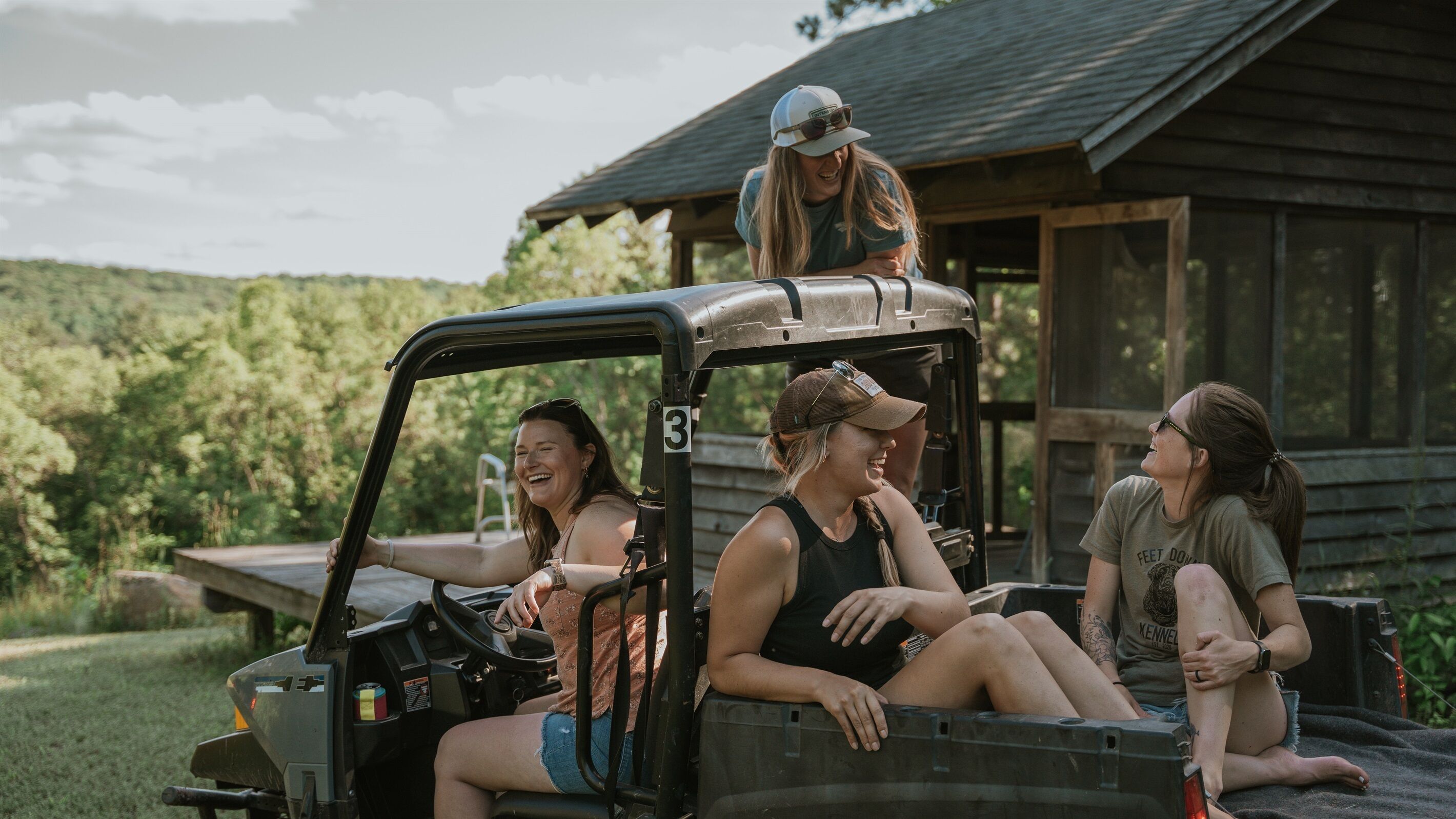 A group of people in a pickup truck parked in front of a wooden cabin.