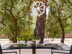 An outdoor dining table with chairs, surrounded by trees and a decorative white structure. - I Ruscioli (Lecce)