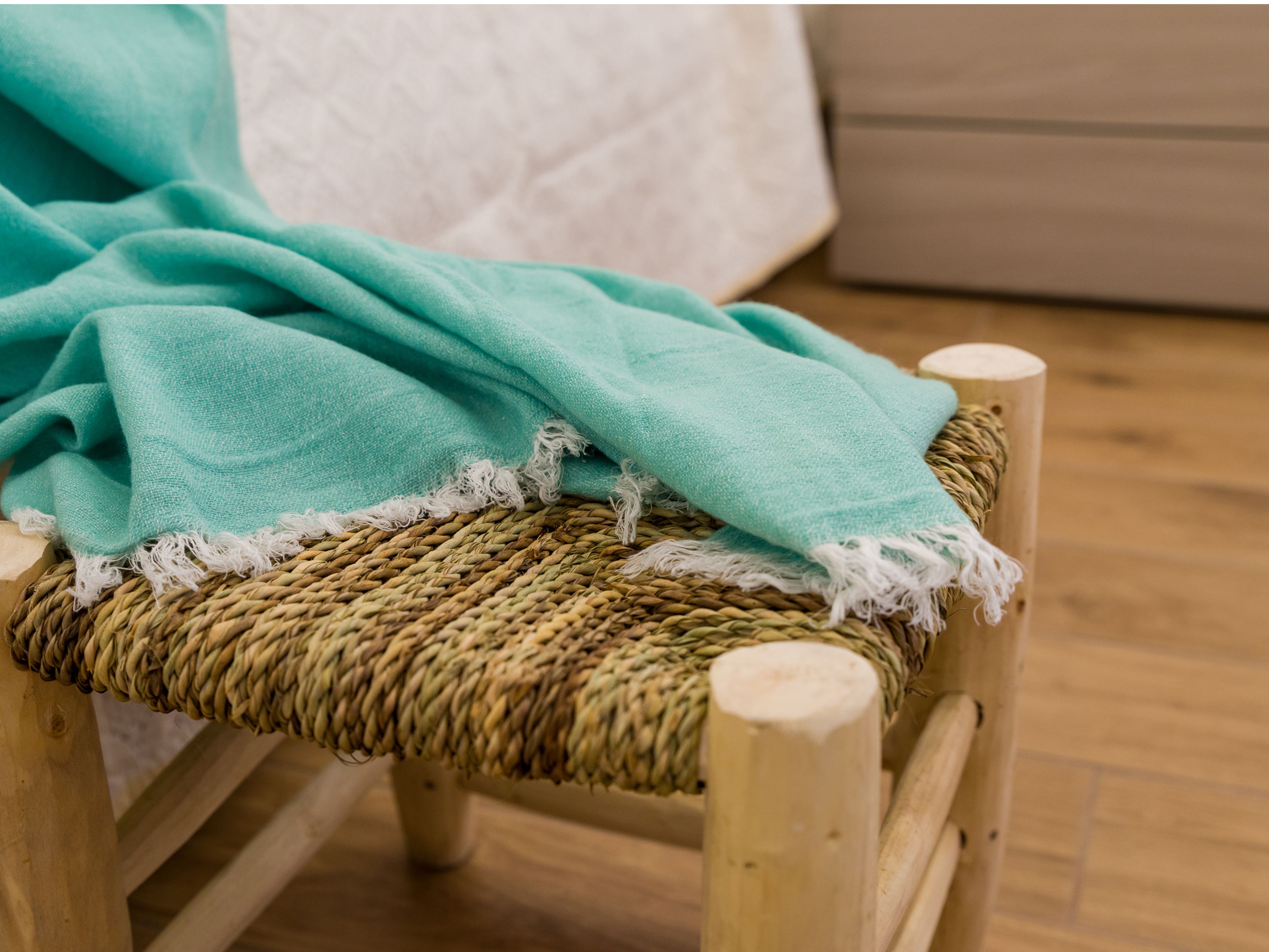 Une chaise en osier recouverte d’un plaid de couleur turquoise.