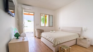 Une chambre à coucher comprenant un lit, des tables de chevet, un bureau, une chaise, un petit tabouret et un téléviseur fixé au mur.