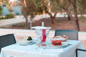 An outdoor dining table with a pitcher, a bowl of greens, and a slice of red meat on a plate.