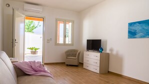 Un salon moderne avec un canapé, un téléviseur posé sur un meuble, un petit fauteuil et une plante en pot.