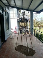 Un espacio al aire libre techado con un arenero, una mesa con sillas y vistas a un edificio de fondo.