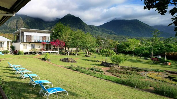 A hotel with a garden view of mountains, a pool with lounge chairs, and a well-maintained lawn. - Moonrise Inn (Donghe)