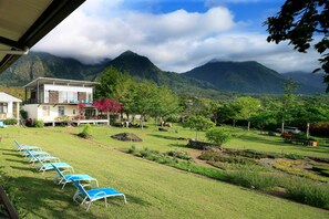Un hotel con vista a las montañas y un jardín, piscina con sillones de descanso y césped bien cuidado.