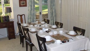 A dining room with a table set for four, chairs, a wooden cabinet, and a window with curtains. - Well Cottage B&B (Cirencester)