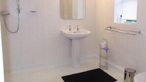 A bathroom with a white sink, a mirror, a shower, and a black rug. - Well Cottage B&B (Cirencester)