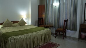 Een keurig opgemaakt bed met een groene sprei, een houten stoel, een klein tafeltje en een lamp.