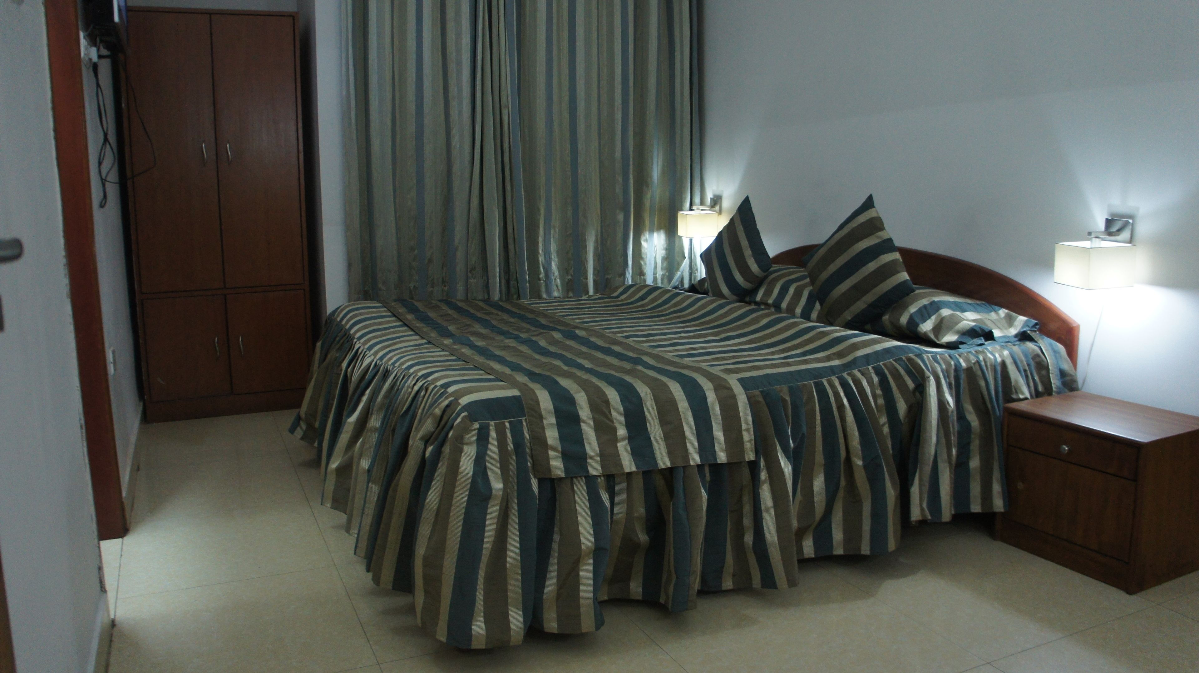 A bedroom with a bed, curtains, a nightstand, and a wardrobe.