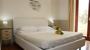 Un dormitorio con cama blanca, dos mesitas de noche con lámparas, un cuadro decorativo con peces y vistas a través de una puerta.
