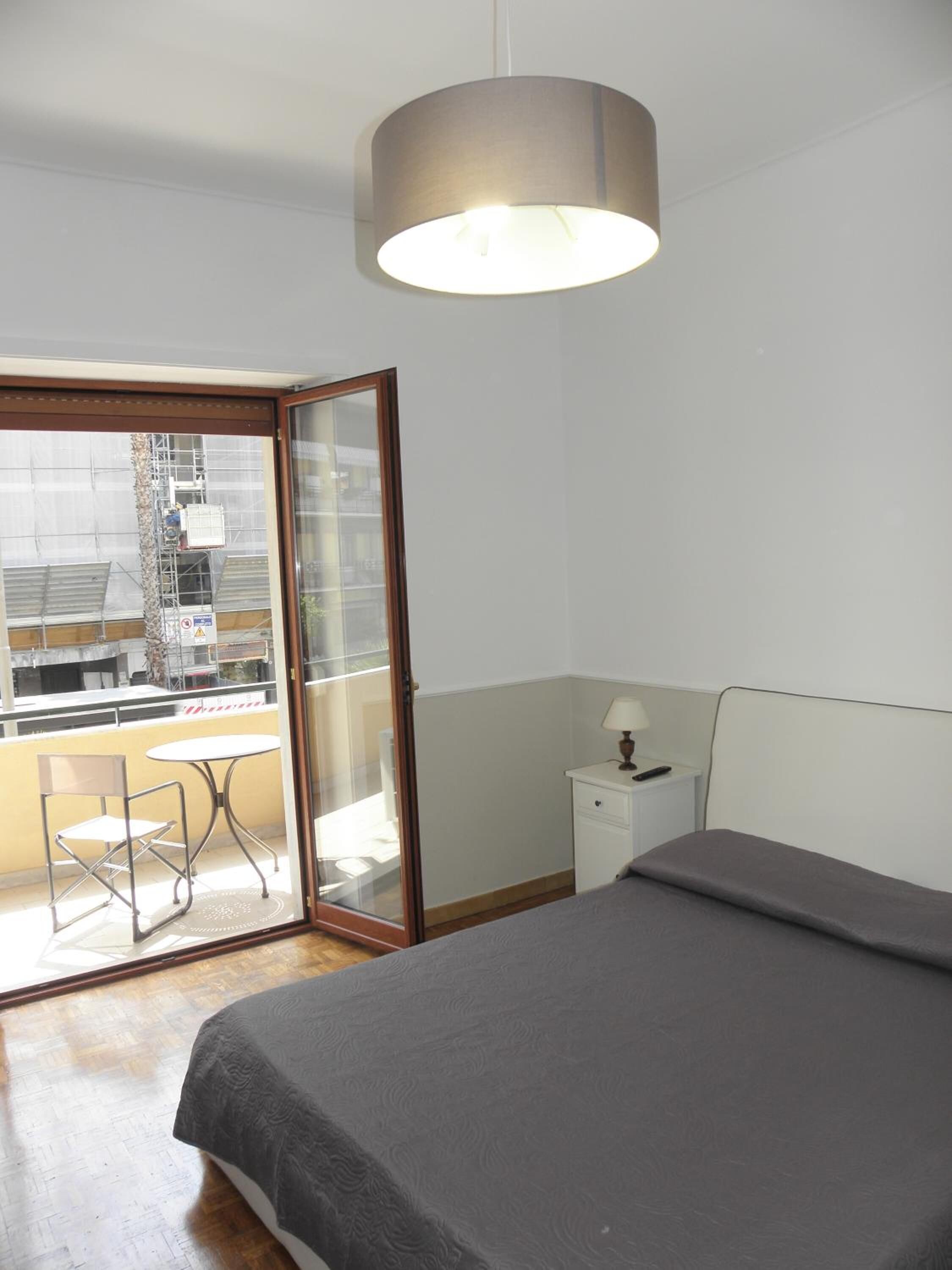A bedroom with a bed, a nightstand, a lamp, a chair, and a table by a sliding glass door.
