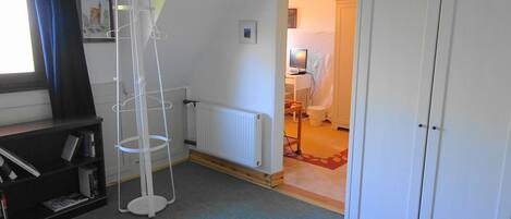A room with a radiator, a white wardrobe, a bookshelf, and a window with curtains.